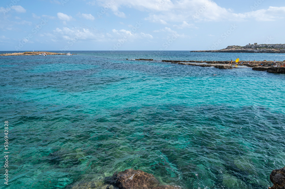 The beautiful Ognina beach in Syracuse with turquoise and green water and a small island in front of it The beautiful Ognina beach in Syracuse with turquoise and green water and a small island in front of it