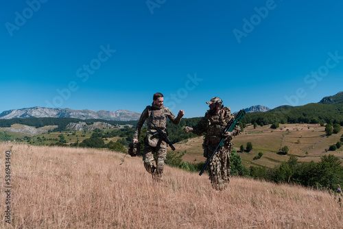A sniper team squad of soldiers is going undercover. Sniper assistant and team leader walking and aiming in nature with yellow grass and blue sky. Tactical camouflage uniform.