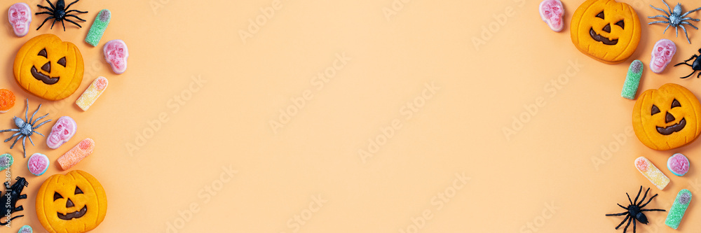 Halloween sweet background frame with scary pumpkin cookies, candy and Halloween decor on orange table Halloween sweet background frame with scary pumpkin cookies, candy and Halloween decor on orange table