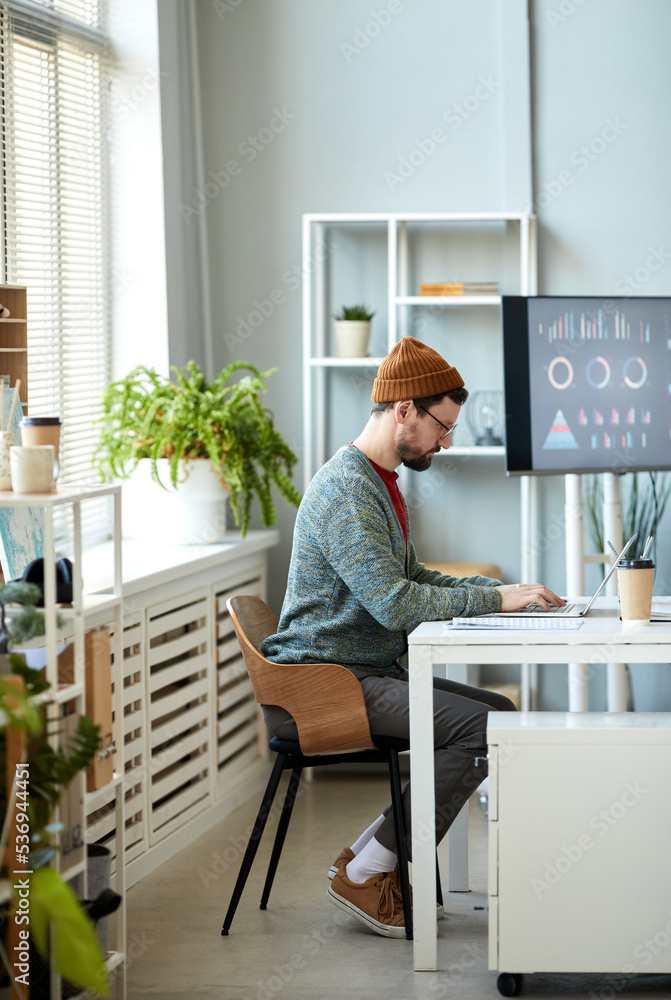 Young serious male office worker sitting by workplace in front of laptop and preparing for project while searching for online information Young serious male office worker sitting by workplace in front of laptop and preparing for project while searching for online information