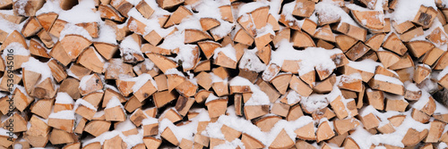textured firewood background chopped wood for kindling and heating. woodpile stacked firewood birch tree covered fresh icy frozen snow and snowflakes. cold weather and snowy winter time season. banner