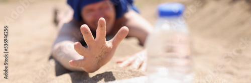 A thirsty man lies on the sand reaching for a bottle of water photo