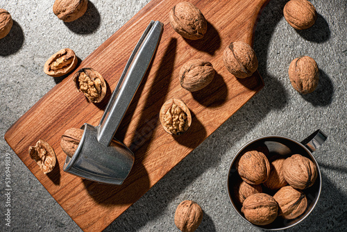 Raw walnuts and a nutcracker on a cutting board. Indoors top view