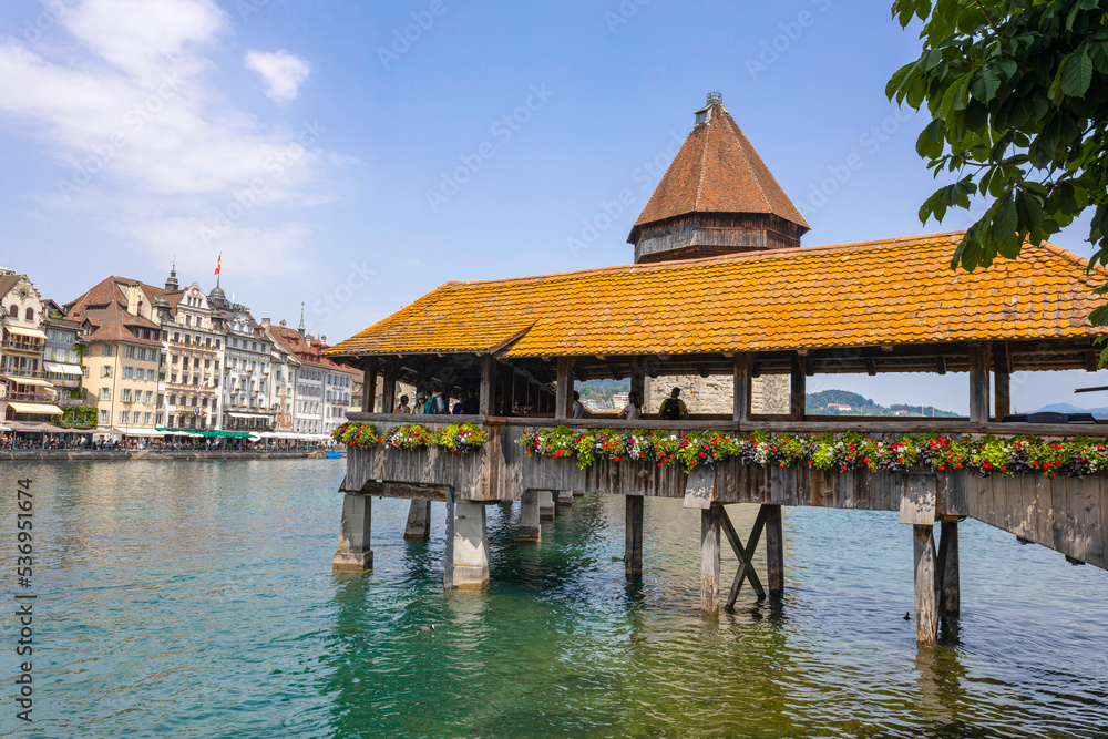 Fototapeta premium LUCERNE, SWITZERLAND, JUNE 21, 2022 - View of the wodden covered Kapellbrucke Bridge on the Reuss river and buildings in city center of Lucerne, Switzerland