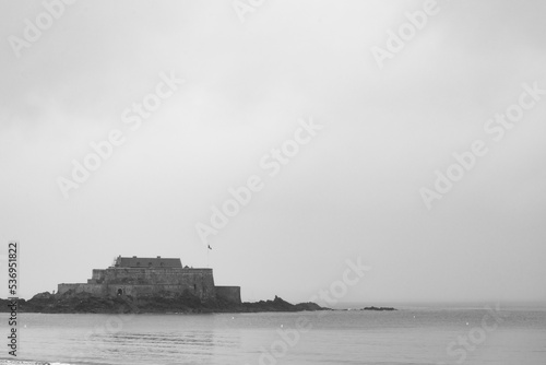 The famous fortress named "Fort du petit bè" in Saint Malo, Brittany, France, during a rainy day. The waters of atlantic ocean in the foreground. Overcasted white sky on the background.