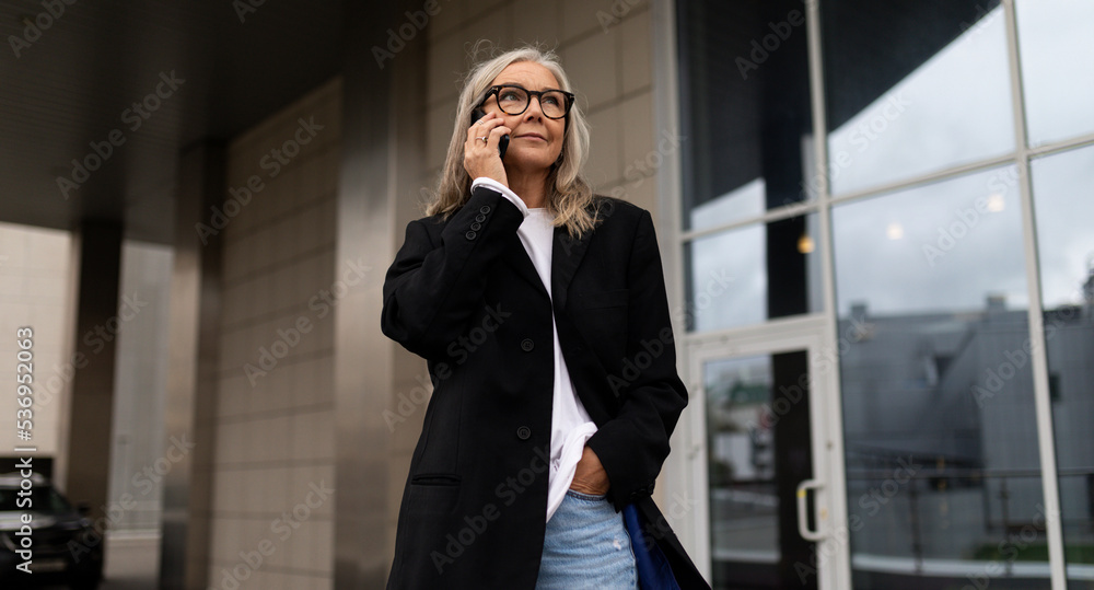 an elderly business woman enters the office center talking on a mobile phone, woman leader in business concept an elderly business woman enters the office center talking on a mobile phone, woman leader in business concept