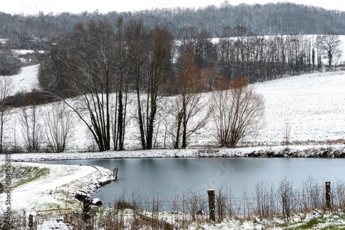 petit étang gelé avec sa glace et entouré d'arbre avec un paysage enneigé par une froide journée d'hiver