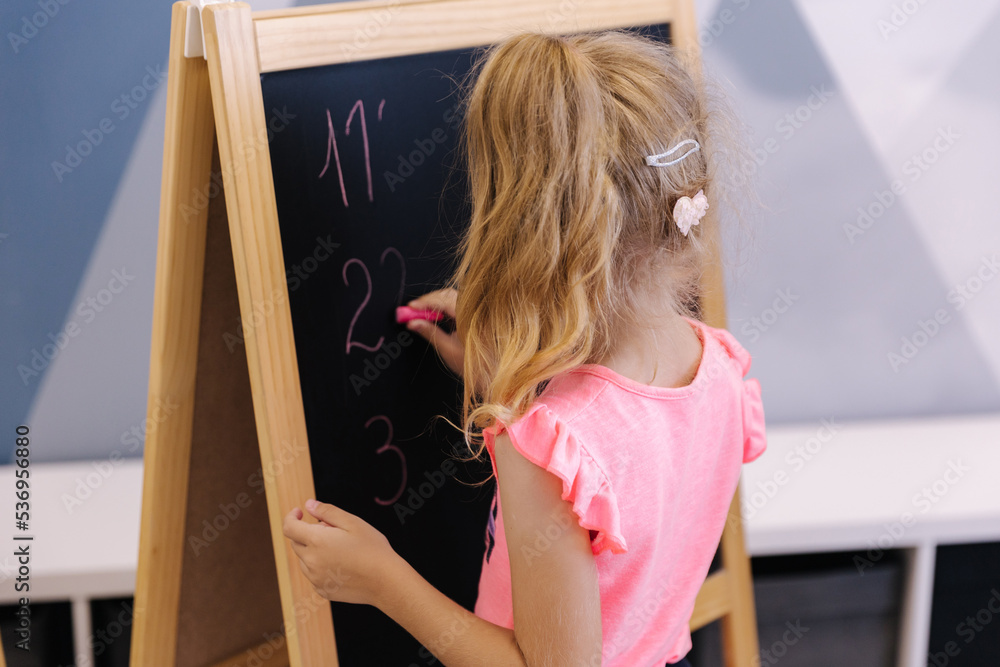 Little girl writes numbers on a board. Kindergarten