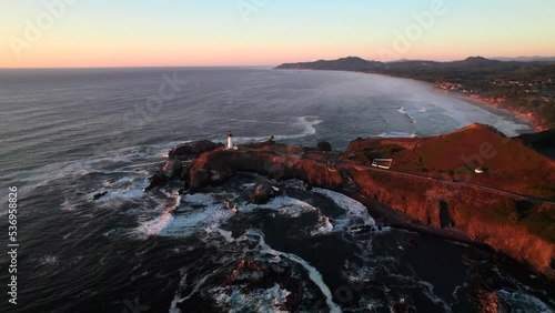 Pacific Northwest coastline with classic Lighthouse, cliffs, and crashing waves. Beautiful sunset aerial footage. photo