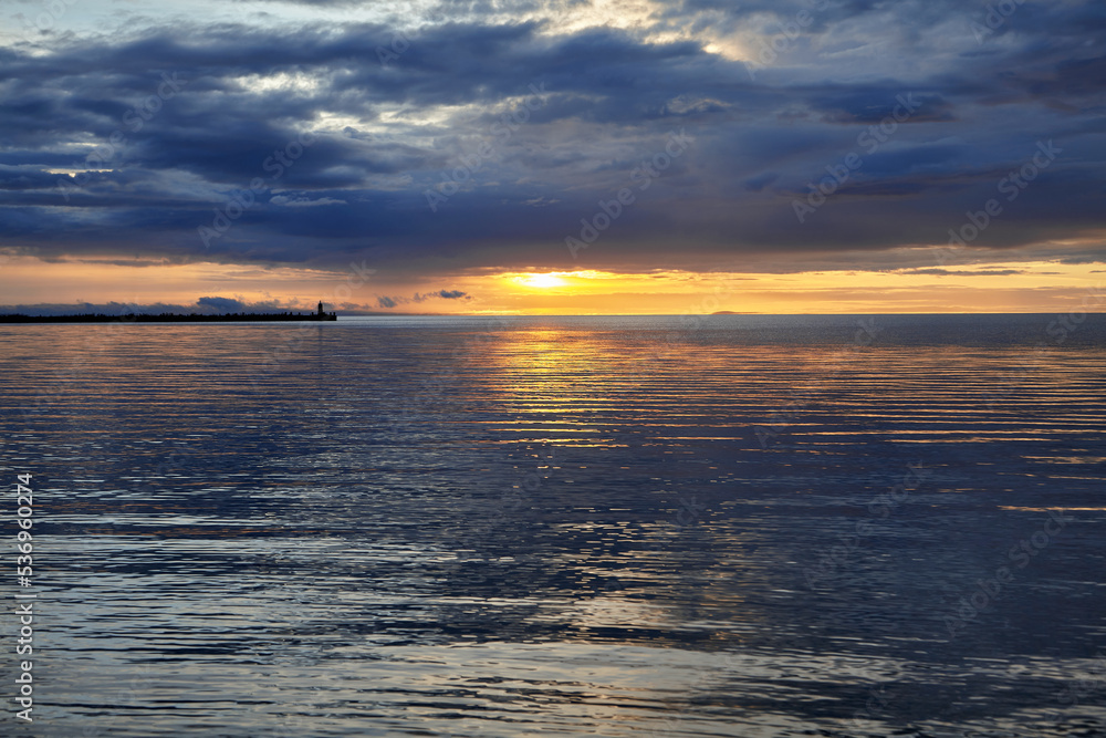 Obraz premium Dramatic sunset with thunderclouds before the storm. Sea pier with a lighthouse against the backdrop of the setting sun