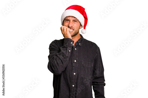 Young caucasian man celebrating Christmas wearing a santa hat isolated biting fingernails, nervous and very anxious.
