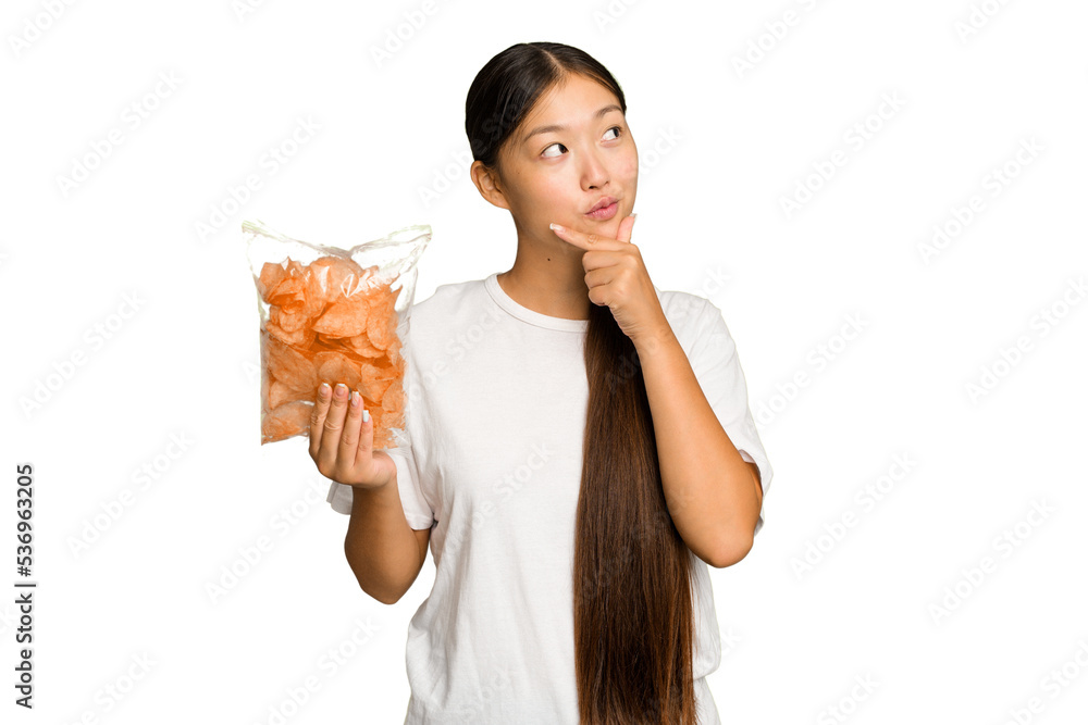 Young asian woman holding crips isolated on green chroma background looking sideways with doubtful and skeptical expression. Young asian woman holding crips isolated on green chroma background looking sideways with doubtful and skeptical expression.