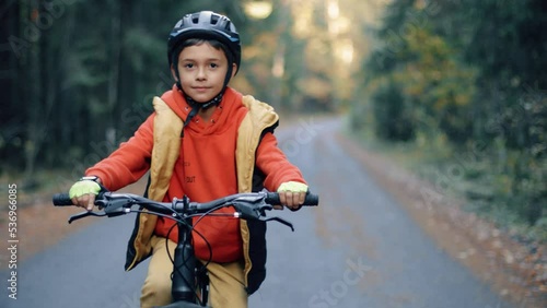 4K kid riding on mountains bike in the forest. Boy in helmets cycling on the autumn nature trail. Active smiling child on bike.
