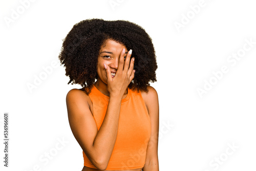 Young African American woman isolated blink at the camera through fingers, embarrassed covering face.