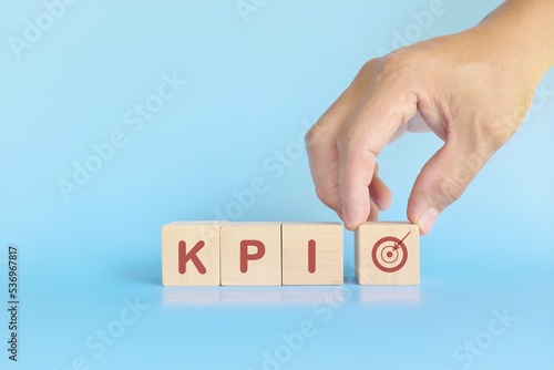 KPI or key performance indicator business target and establishment concept. Human hand stacking wooden blocks in blue background.