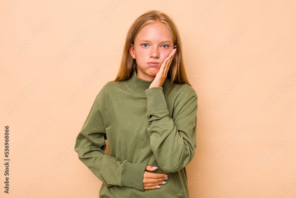 Caucasian teen girl isolated on beige background blows cheeks, has tired expression. Facial expression concept. Caucasian teen girl isolated on beige background blows cheeks, has tired expression. Facial expression concept.