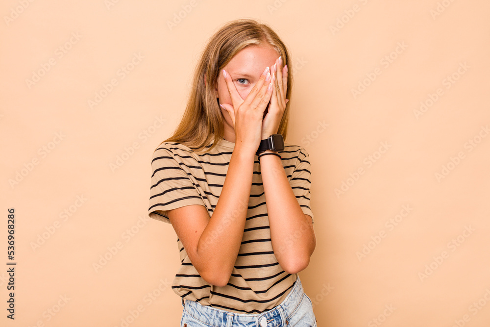 Caucasian teen girl isolated on beige background blink through fingers frightened and nervous. Caucasian teen girl isolated on beige background blink through fingers frightened and nervous.