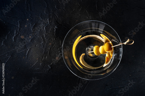 Martini, a glass with spicy olives on a toothpick, on a black background. Alcoholic cold drink, overhead shot with a place for text