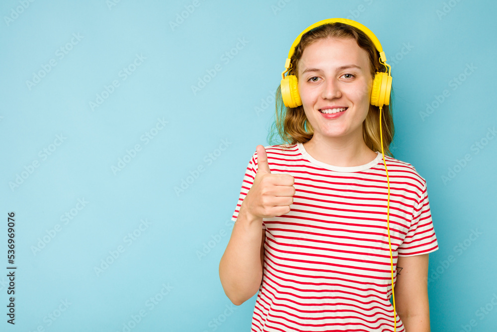 Young caucasian woman wearing headphones isolated on blue background smiling and raising thumb up Young caucasian woman wearing headphones isolated on blue background smiling and raising thumb up