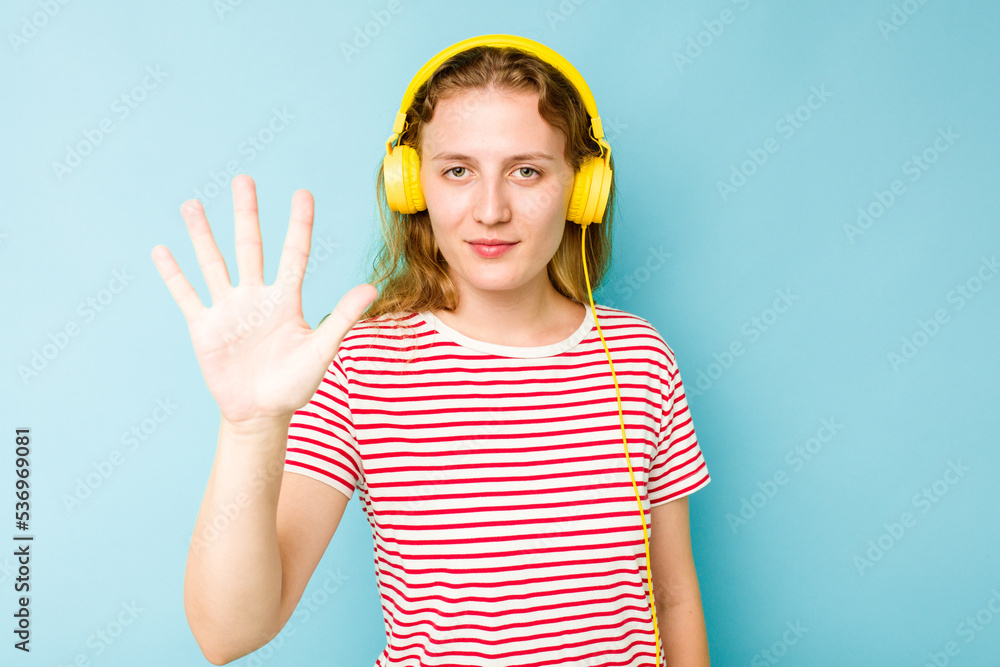 Young caucasian woman wearing headphones isolated on blue background smiling cheerful showing number five with fingers. Young caucasian woman wearing headphones isolated on blue background smiling cheerful showing number five with fingers.