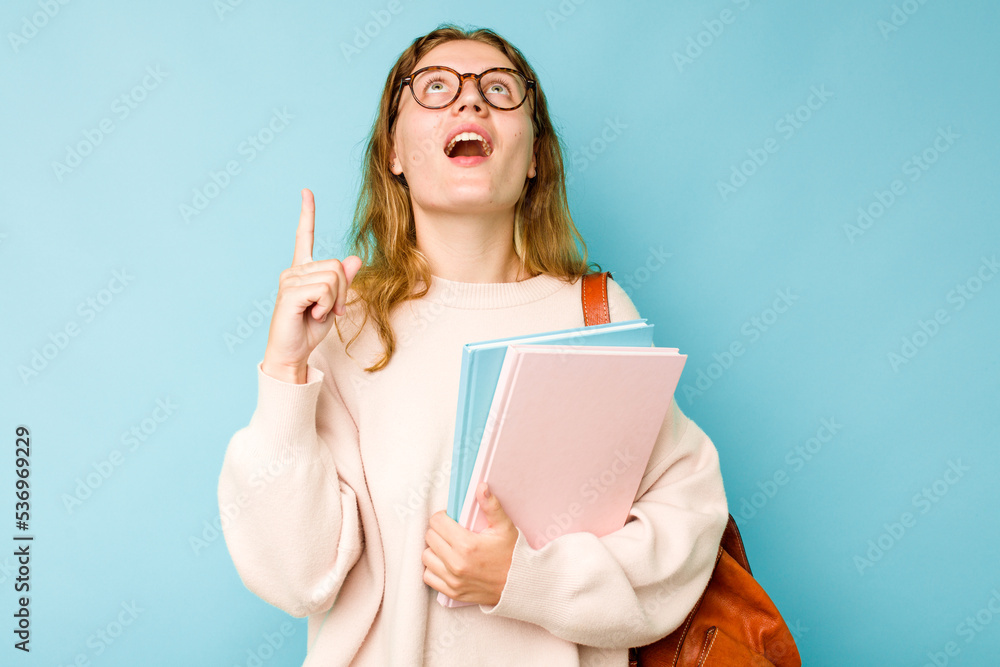Young student caucasian woman isolated on blue background pointing upside with opened mouth. Young student caucasian woman isolated on blue background pointing upside with opened mouth.