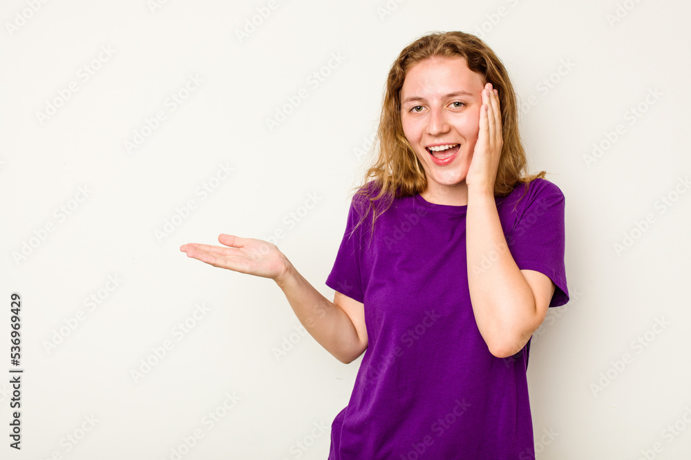 Young caucasian woman isolated on white background holds copy space on a palm, keep hand over cheek. Amazed and delighted. Young caucasian woman isolated on white background holds copy space on a palm, keep hand over cheek. Amazed and delighted.