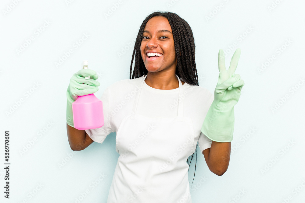 Young African American cleaner woman isolated on blue background joyful and carefree showing a peace symbol with fingers.