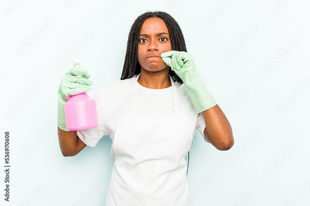 Young African American cleaner woman isolated on blue background with fingers on lips keeping a secret. Young African American cleaner woman isolated on blue background with fingers on lips keeping a secret.