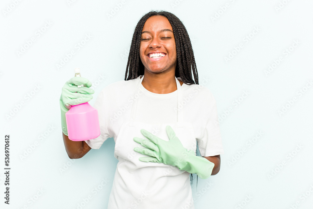 Young African American cleaner woman isolated on blue background laughs out loudly keeping hand on chest. Young African American cleaner woman isolated on blue background laughs out loudly keeping hand on chest.