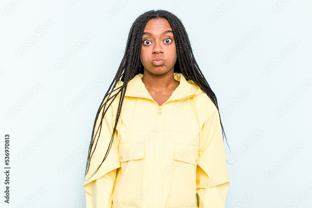 Young African American woman with braids hair isolated on blue background blows cheeks, has tired expression. Facial expression concept. Young African American woman with braids hair isolated on blue background blows cheeks, has tired expression. Facial expression concept.