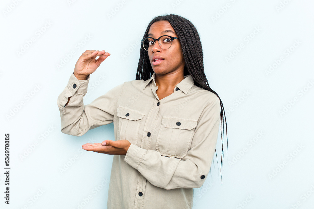 Young African American woman with braids hair isolated on blue background holding something with both hands, product presentation. Young African American woman with braids hair isolated on blue background holding something with both hands, product presentation.