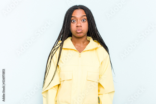 Young African American woman with braids hair isolated on blue background blows cheeks, has tired expression. Facial expression concept. © Asier