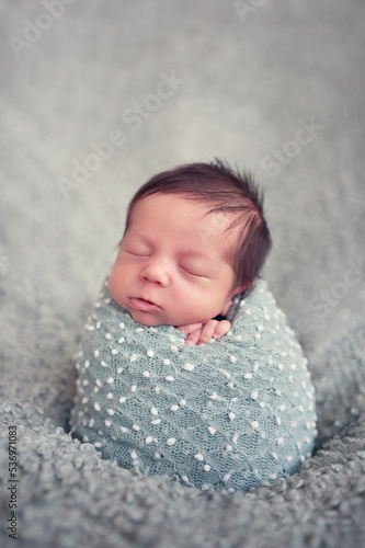 Portrait of newborn baby boy wrapped in blue wrap. Infant sleeping. Newborn baby with beautiful long dark hair.