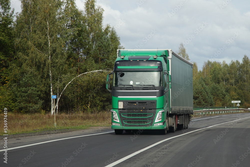 Green semi truck drive on countryside highway road front view. Goods import in Europe Green semi truck drive on countryside highway road front view. Goods import in Europe