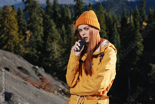 A young woman smokes an e-cigarette in the mountains while hiking