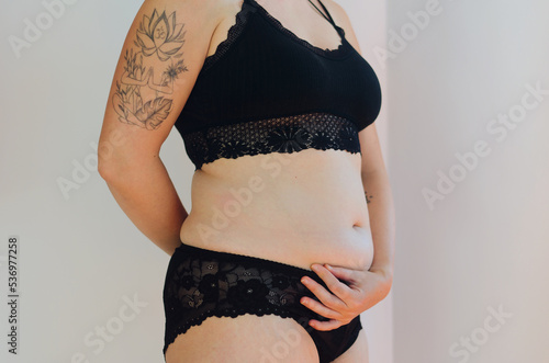 Tattooed woman in black underwear with fat belly, overweight female body isolated on white background. Lose weight. concept of surgery, subcutaneous fat breakdown.