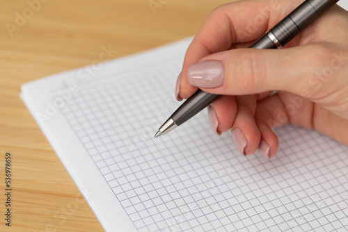 Elegant female hand with a pen over a white sheet of paper. The woman writes with a pen. Premium pen in a female hand. Elegant female hand with perfect manicure. Symbol of business and office work. 