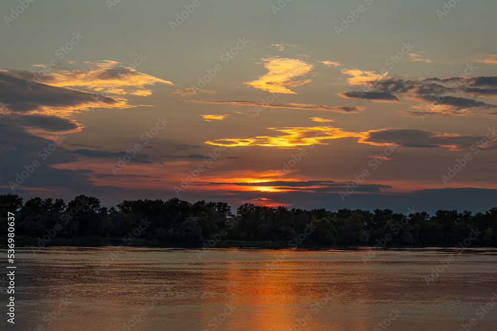 Beautiful sunset over the Dnieper river and forest in Ukraine. Picturesque yellow and golden clouds