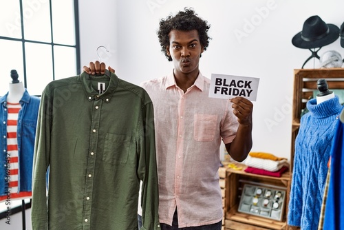 African man with curly hair holding black friday banner at retail shop looking at the camera blowing a kiss being lovely and sexy. love expression.