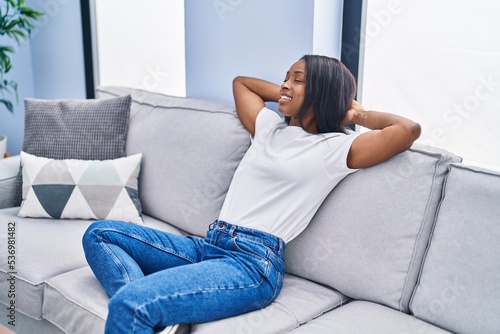 Young african american woman relaxed with hands on head sitting on sofa at home