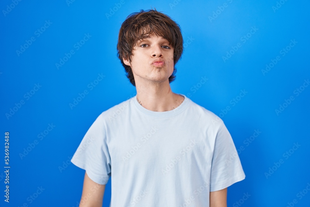 Hispanic young man standing over blue background looking at the camera blowing a kiss on air being lovely and sexy. love expression. Hispanic young man standing over blue background looking at the camera blowing a kiss on air being lovely and sexy. love expression.