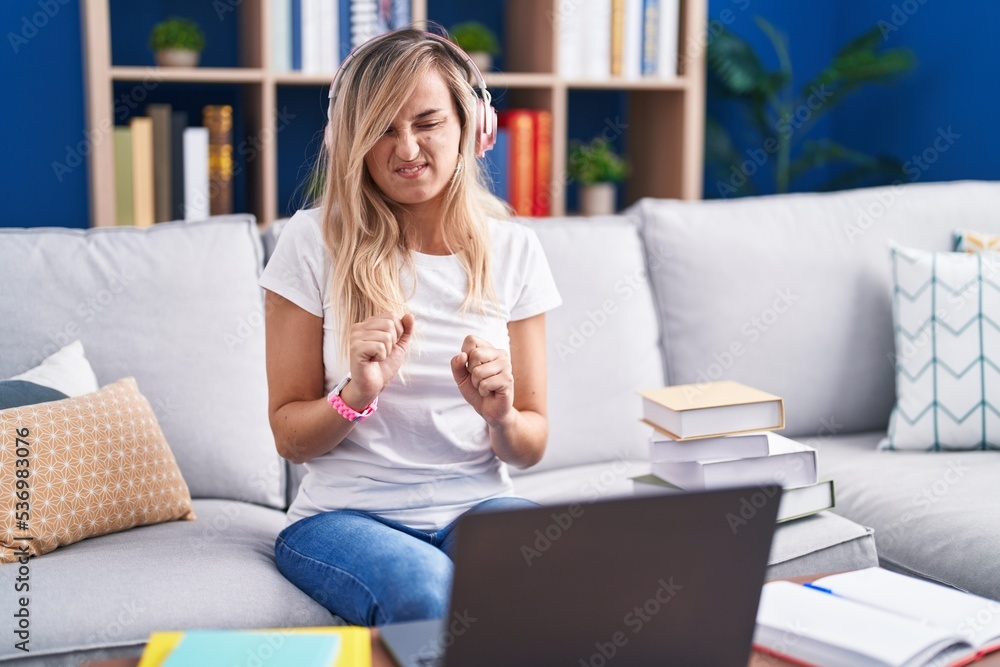 Young blonde woman studying using computer laptop at home disgusted expression, displeased and fearful doing disgust face because aversion reaction. Young blonde woman studying using computer laptop at home disgusted expression, displeased and fearful doing disgust face because aversion reaction.
