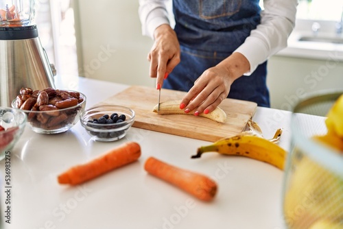 Young blonde woman cutting banana at kitchen