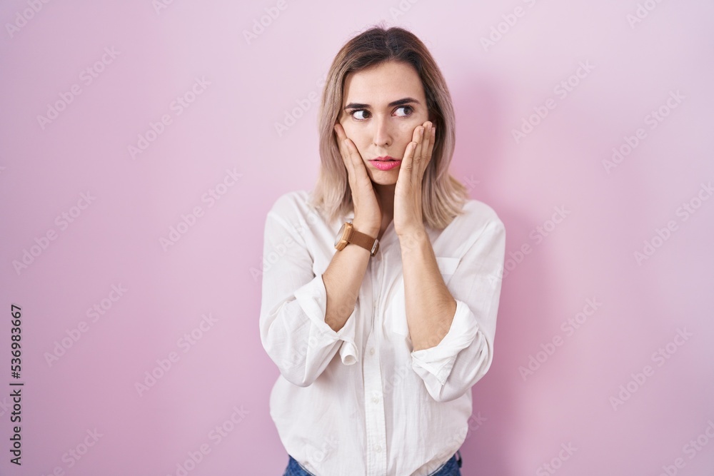 Young beautiful woman standing over pink background tired hands covering face, depression and sadness, upset and irritated for problem Young beautiful woman standing over pink background tired hands covering face, depression and sadness, upset and irritated for problem