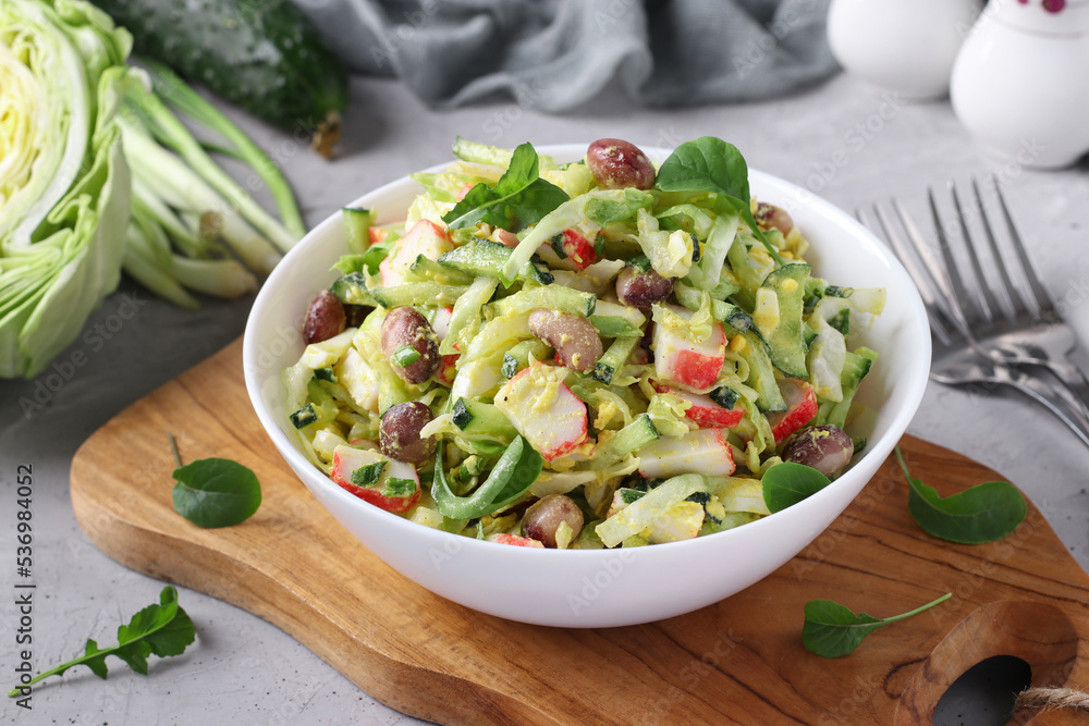 Salad with cabbage, crab sticks, beans, eggs and cucumber in white bowl on wooden board Salad with cabbage, crab sticks, beans, eggs and cucumber in white bowl on wooden board