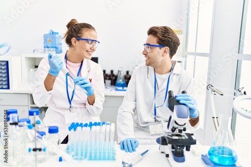 Man and woman wearing scientist uniform using pipette and microscope working at laboratory
