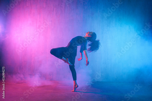 Fototapeta Naklejka Na Ścianę i Meble -  Modern dance girl dancer dancing in neon light doing gymnastic exercises in studio, copy space.