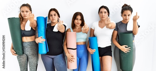 Group of women holding yoga mat standing over isolated background showing middle finger, impolite and rude fuck off expression