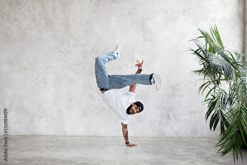 B-Boy performing one handed freeze. Guy breakdancer stands on arm and lifted legs up. Hip hop dance photo