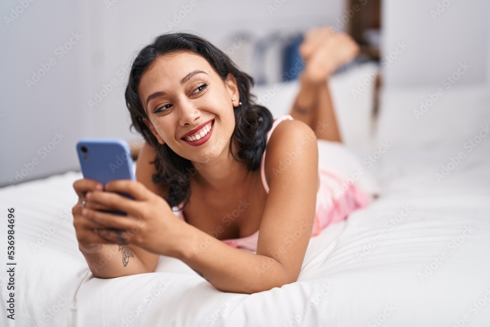 Young beautiful hispanic woman using smartphone lying on bed at bedroom Young beautiful hispanic woman using smartphone lying on bed at bedroom